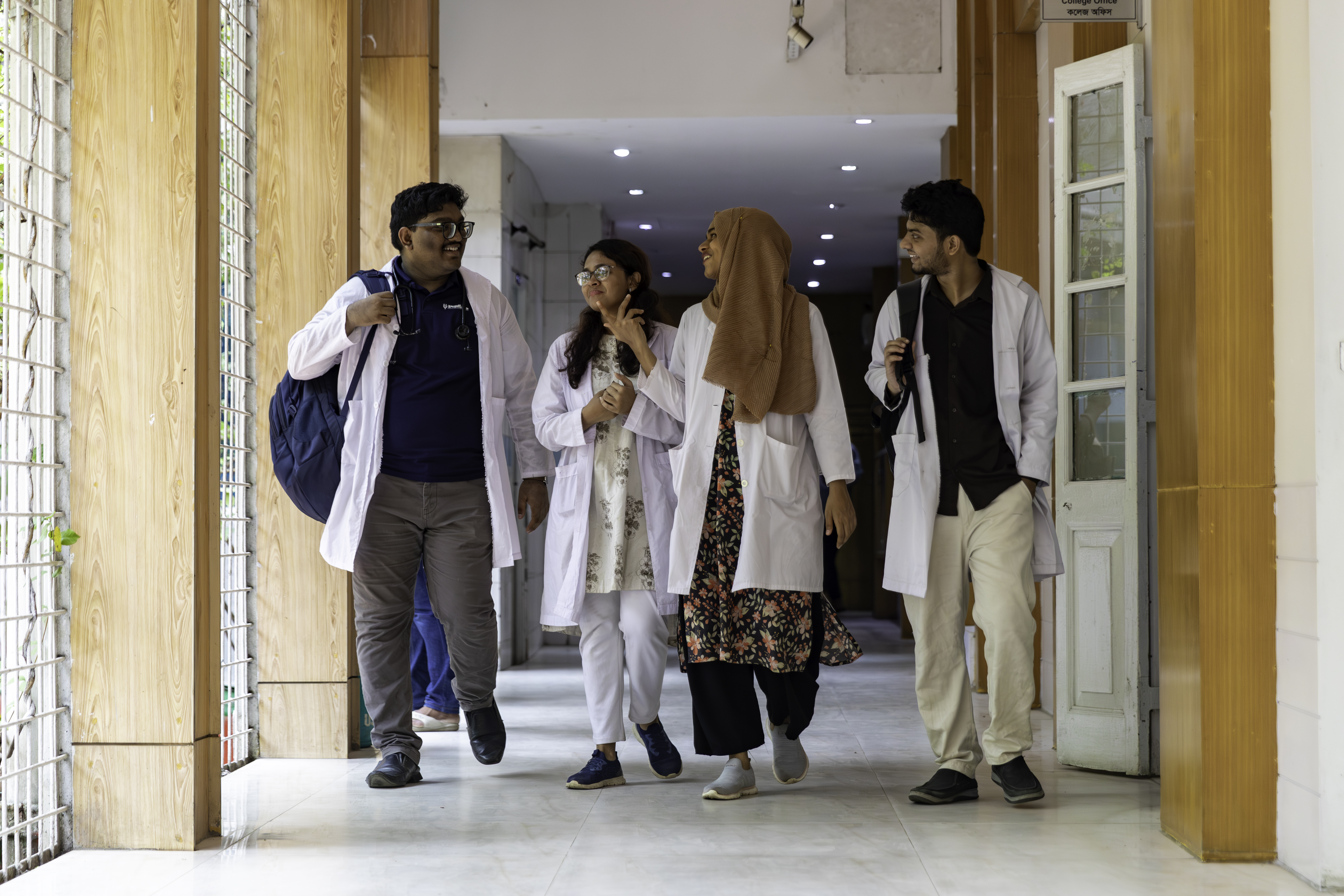 Medical interns walking down the hallway of a hospital while conversing with each other. 